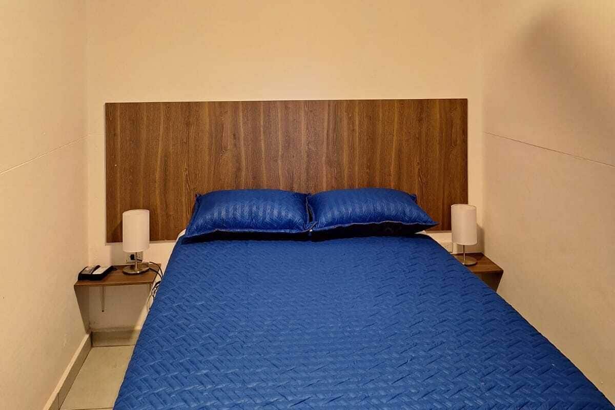 A bedroom with a bed, a wooden headboard, two bedside tables with lamps, and a ceiling fan.