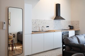 A compact kitchen with white cabinets, a black range hood, and a speckled backsplash.