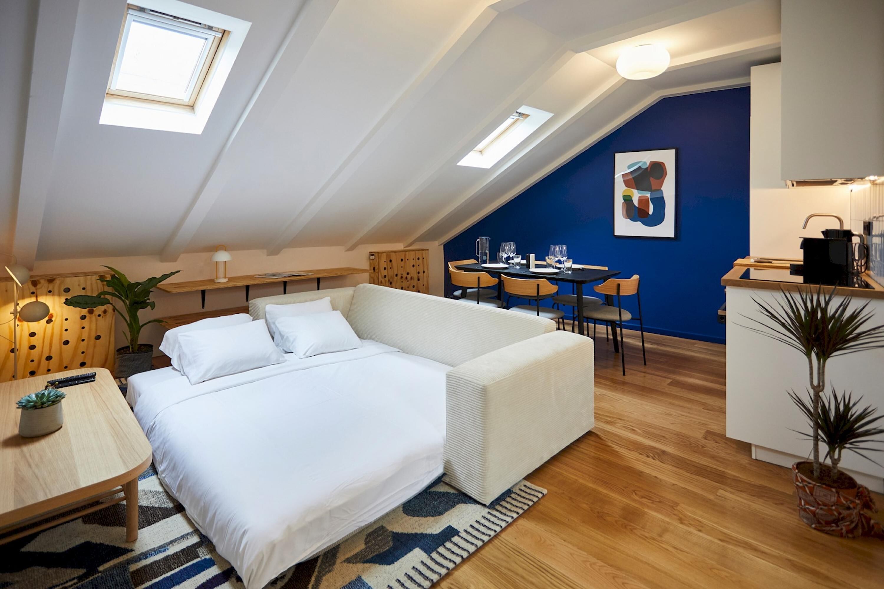 Une chambre moderne de style loft, avec un canapé-lit blanc, une table à manger en bois et un coin cuisine.