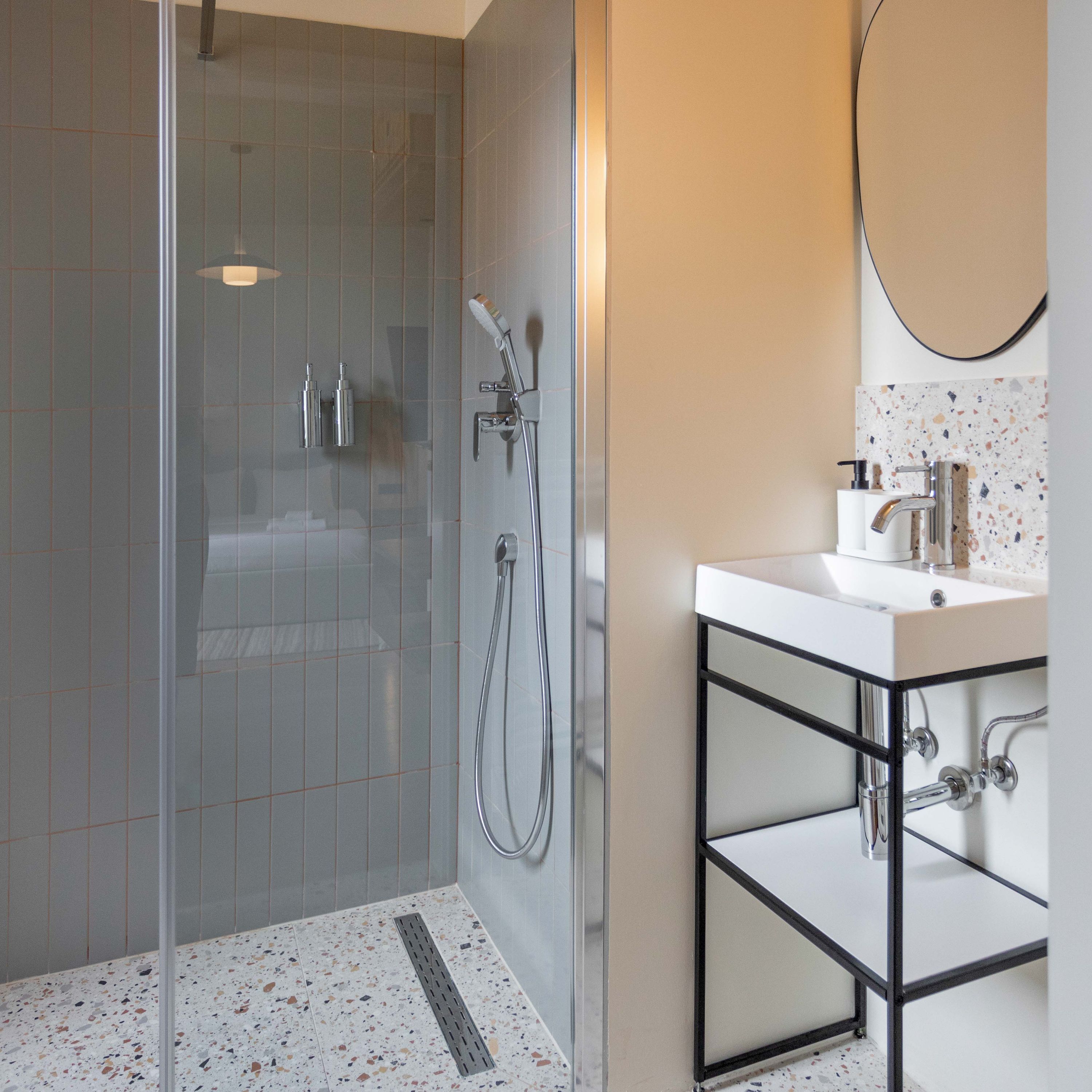 A modern bathroom with a glass-enclosed shower, a white sink with a black frame, and a speckled tile floor.