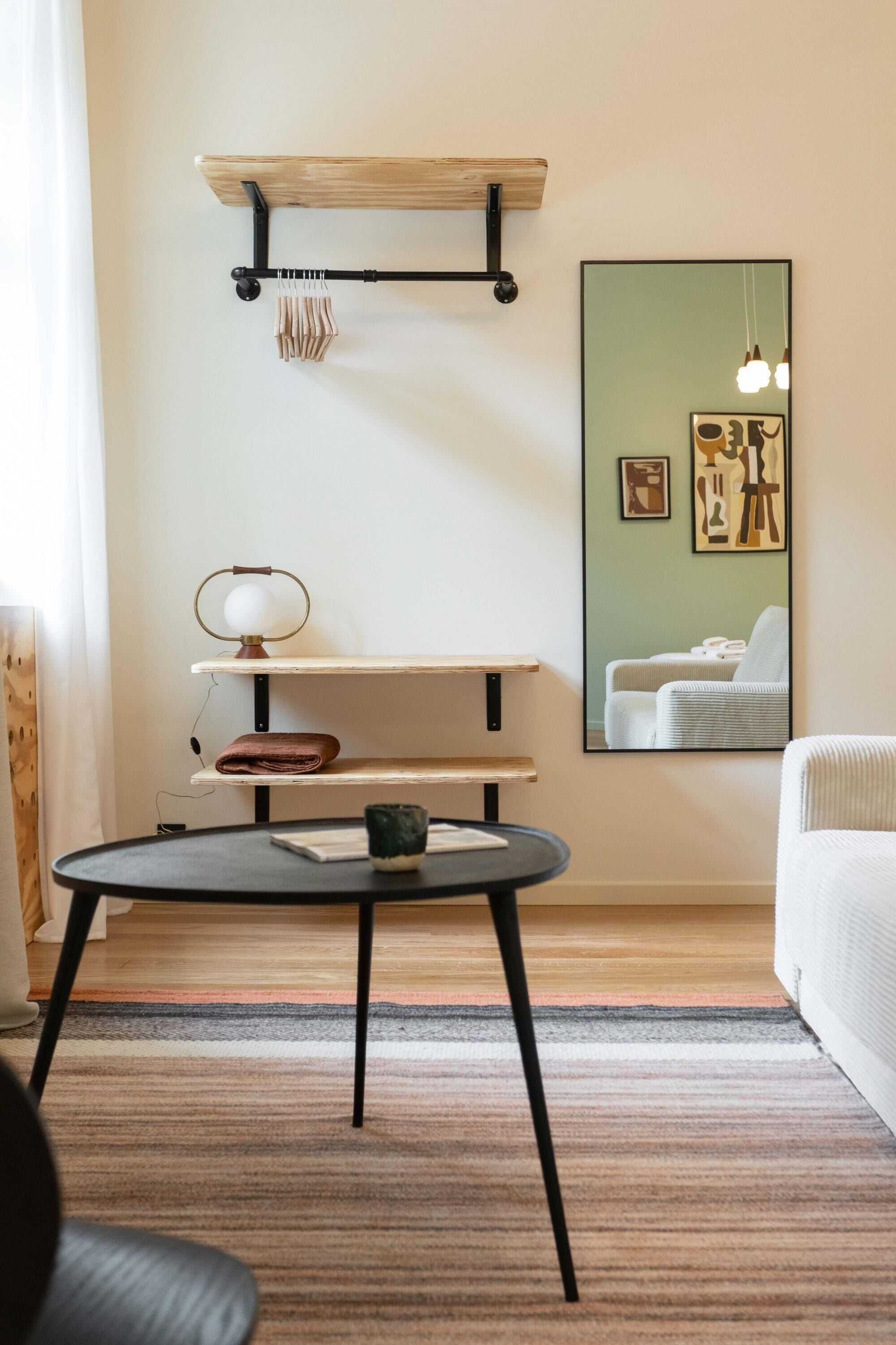 A modern living room with a round table, a wooden shelf unit, and a large mirror on the wall.