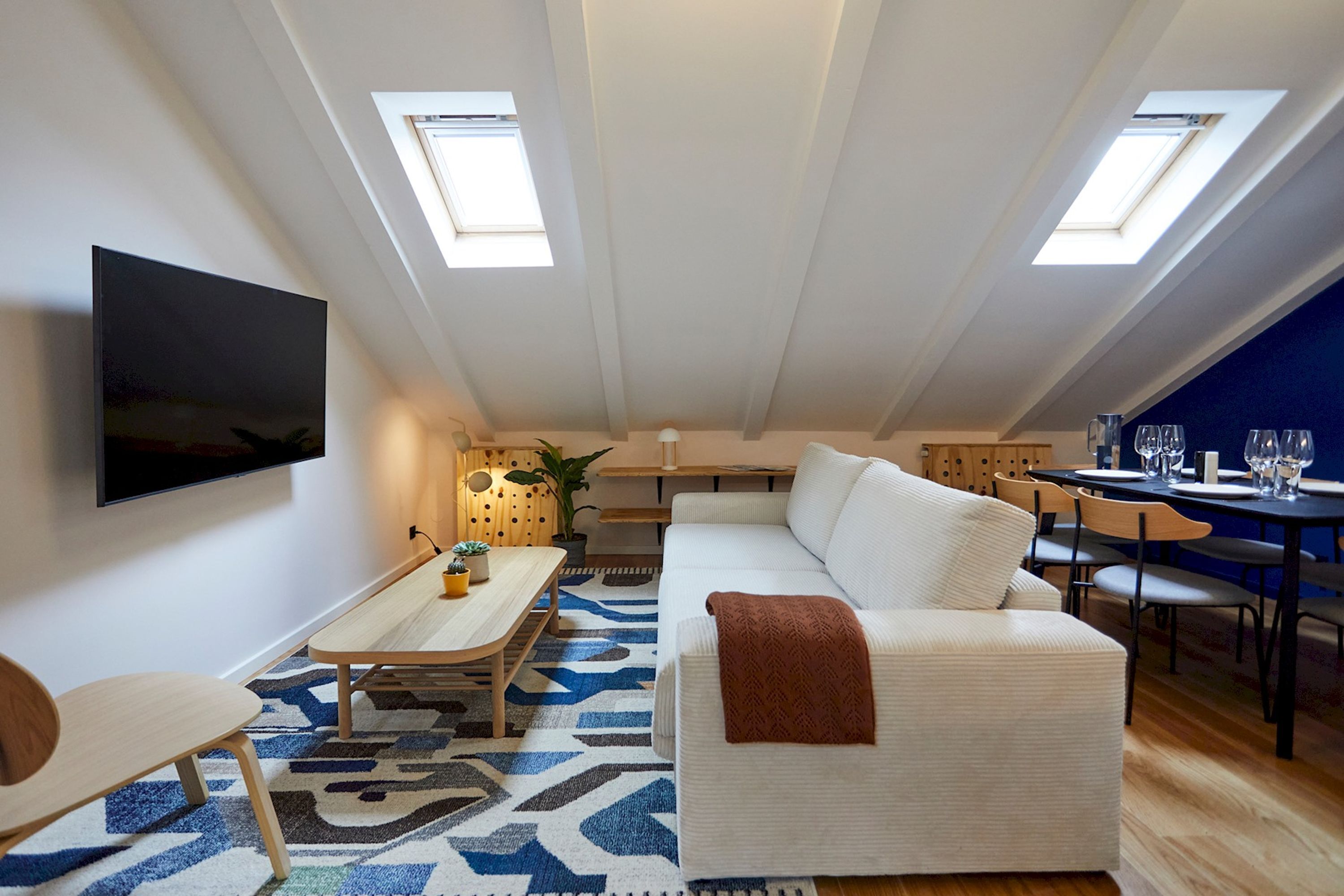 A modern loft apartment with a living area featuring a sofa, a dining table, and a TV mounted on the wall.