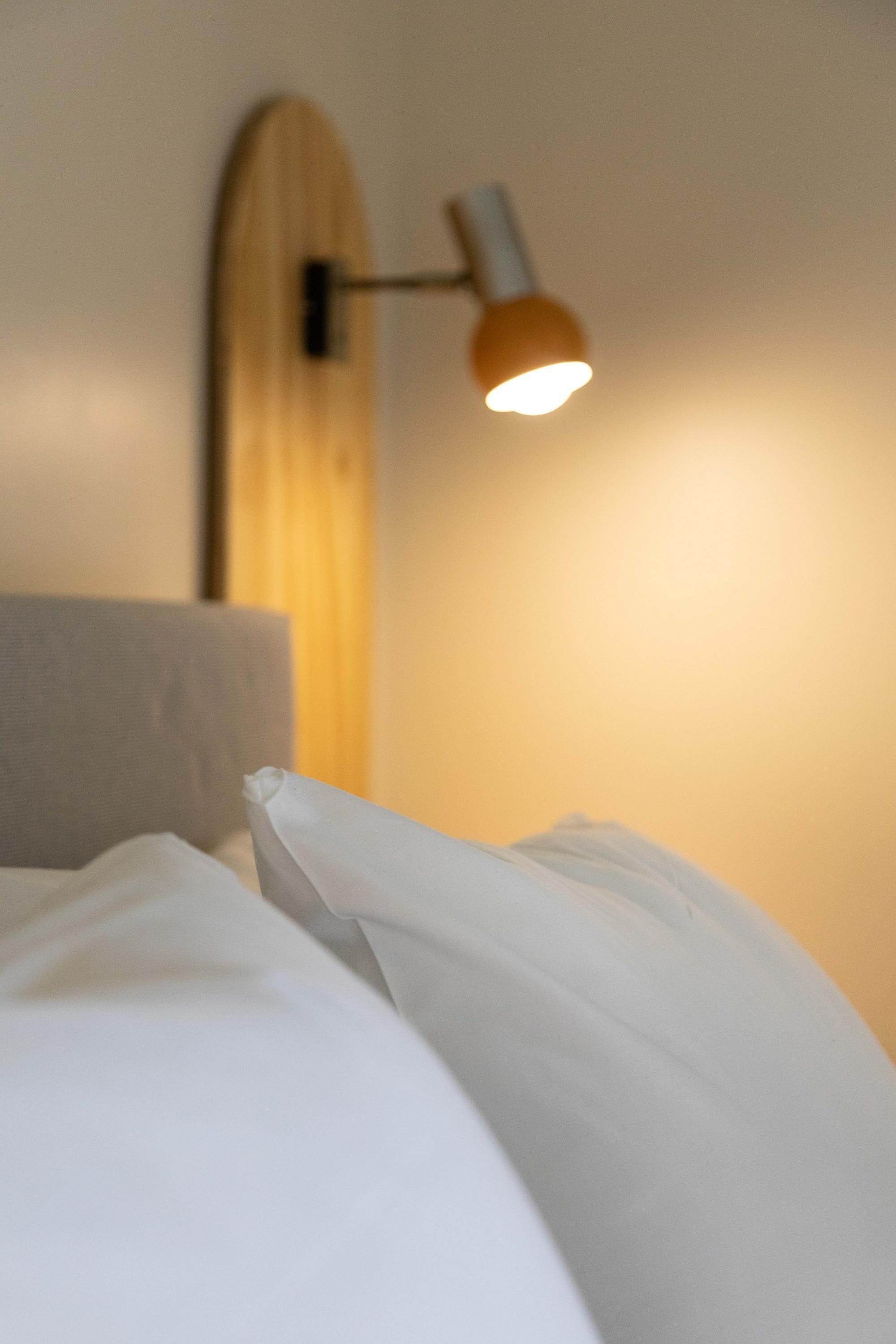 A bed with white bedding and a wall-mounted lamp.