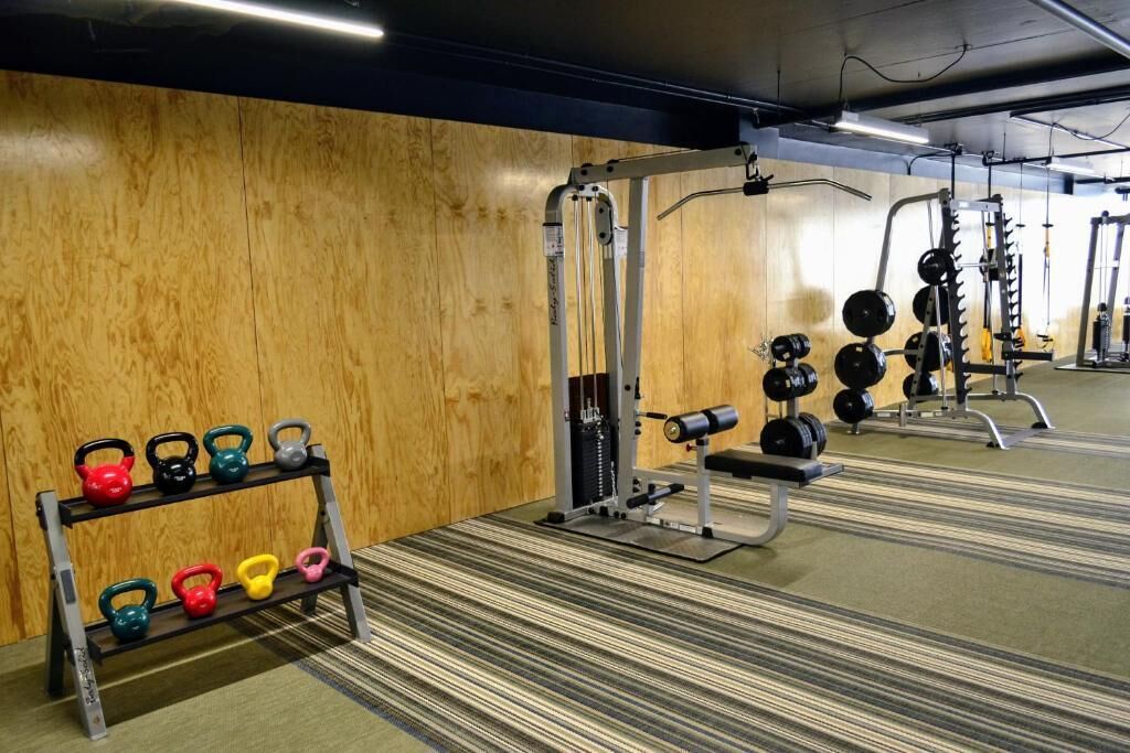 A gym with weightlifting equipment, a bench, and a rack of kettlebells.