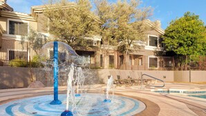 A water fountain with multiple jets, surrounded by a tiled area with lounge chairs and a pool. - WorldMark South Mountain Preserve - 2 Bedroom Accessible (Phoenix)