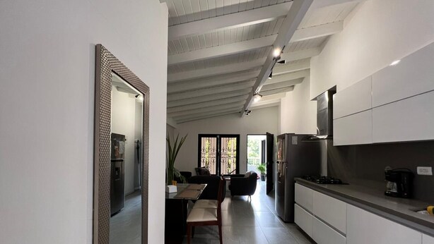 Une cuisine moderne avec des meubles blancs, un coin repas comprenant une table et des chaises, et un grand miroir au mur.