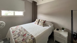 Une chambre à coucher comprenant un lit, une table de chevet, une commode, une fenêtre et un ventilateur de plafond.