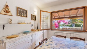 A room with a dining table, white cabinets, a window with a view of a garden, and nautical-themed decor. - Terraced house with swimming pool (Tertenia)