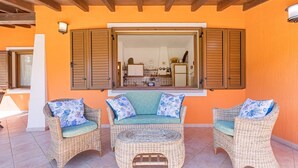 A wicker furniture set with cushions, a window with shutters, and a tiled floor. - Terraced house with swimming pool (Tertenia)