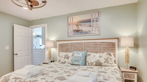 A bedroom with a bed featuring a nautical-themed bedspread, a beach-themed pillow, and a view of the ocean through a window. - St Helena Island Condo w/ Beach Views & Porch! (St Helena Island)