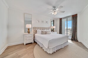 A bedroom with a large bed, a ceiling fan, and a view of the outdoors.