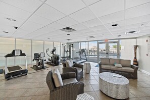 A gym with exercise equipment, a treadmill, and a lounge area with a sofa and ottoman.