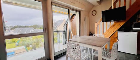 Una cocina moderna con una escalera de madera, un comedor con sillas blancas y un amplio ventanal con vistas al vecindario.