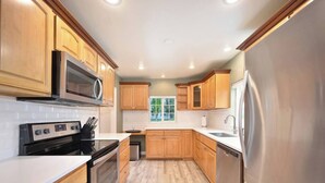 A modern kitchen with wooden cabinets, stainless steel appliances, and a window providing natural light. - Sanders Beach Retreat, walk to DT & Sanders beach! (Coeur d'Alene)