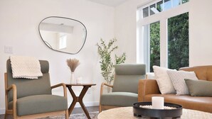 A modern living room with two armchairs, a round coffee table, and a sofa. There is a mirror on the wall and a window providing natural light. - Sanders Beach Retreat, walk to DT & Sanders beach! (Coeur d'Alene)