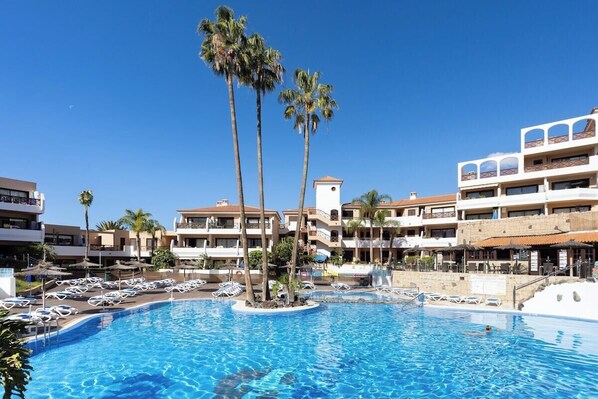 A swimming pool with lounge chairs, palm trees, and a multi-story hotel building.