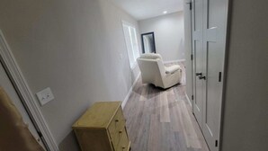 Ein Flur mit einem beigefarbenen Sessel, einer Holzkommode und einer Tür mit Spiegel.