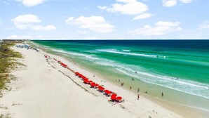 A beach with a row of red umbrellas, clear turquoise water, and a sandy shore.
