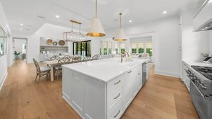A modern kitchen with white cabinetry, a large island, pendant lighting, and a dining area with chairs.