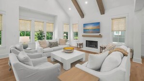 A spacious living room with a fireplace, large windows, and a view of greenery outside.