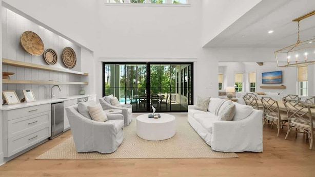 A spacious living area with white furniture, a round coffee table, and a dining area with wooden chairs.