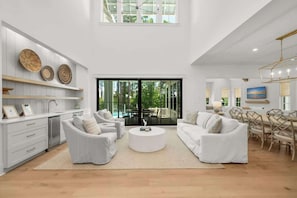 A spacious living area with white furniture, a round coffee table, and a dining area with wooden chairs.