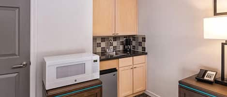 Una cocina compacta con microondas, cafetera y un refrigerador pequeño.