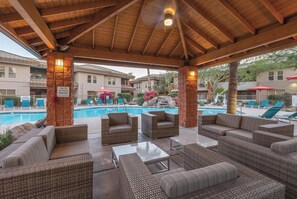 A covered outdoor seating area with wicker furniture, a pool, and a sign indicating emergency contact information.