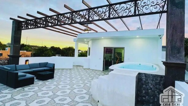 Una terraza en la azotea con un sofá exterior negro, una bañera de hidromasaje y una pérgola.