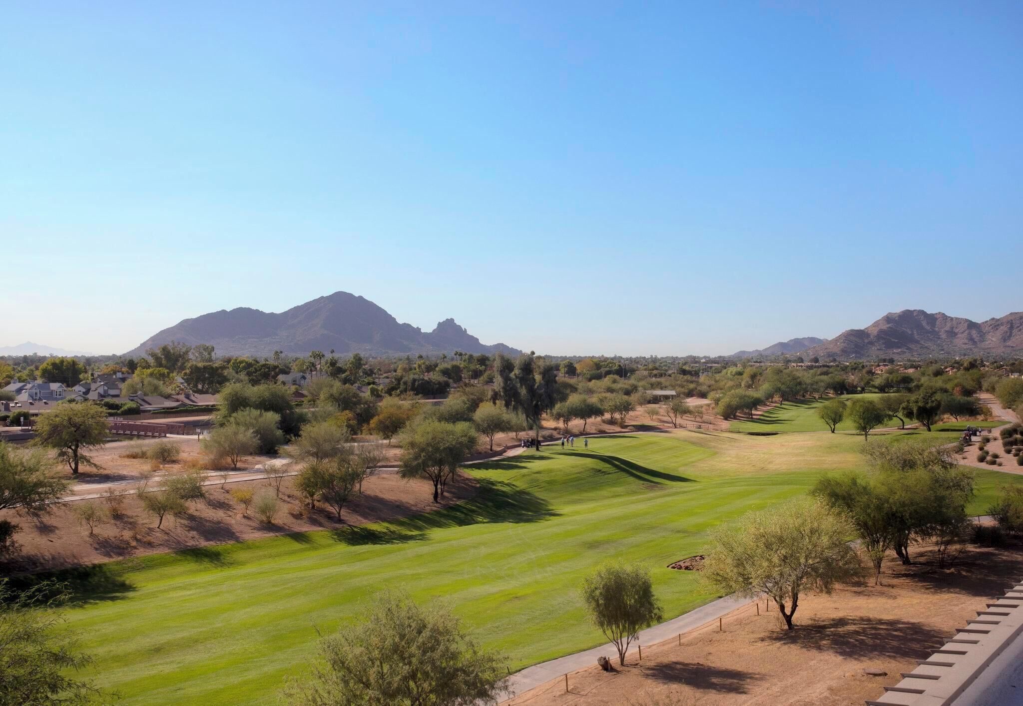 Un campo de golf con vistas despejadas del paisaje circundante, incluyendo montañas distantes y vegetación escasa.
