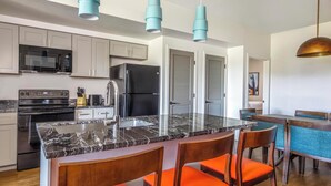 A modern kitchen with a central island, stainless steel appliances, and teal pendant lights. - WorldMark Scottsdale - 2 Bedroom Presidential Accessible (Scottsdale)