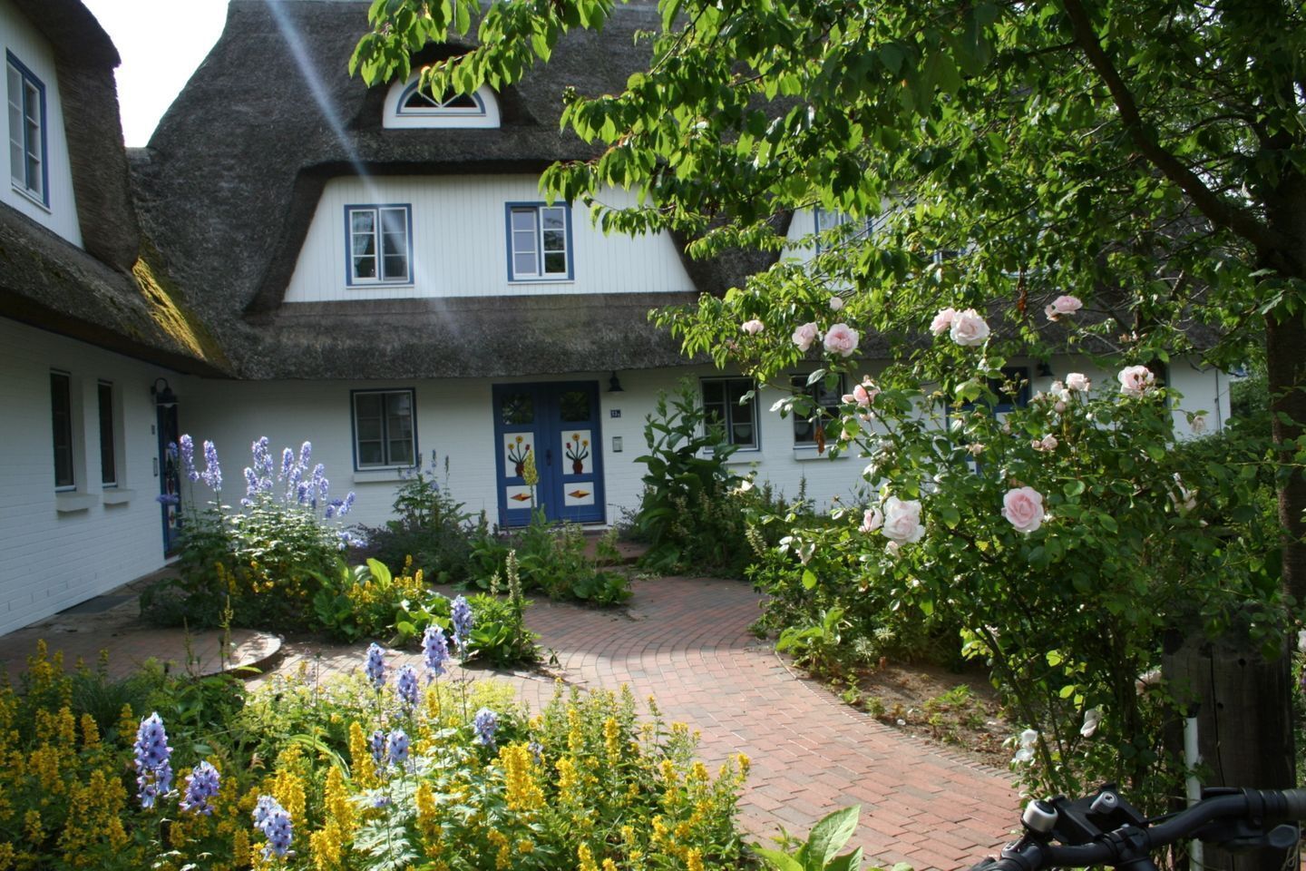 A traditional building with a thatched roof, a blue door, and a garden with flowers and a bicycle.