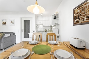 Una cocina moderna con armarios blancos, una mesa de comedor de madera dispuesta para cuatro comensales y un tostador blanco.