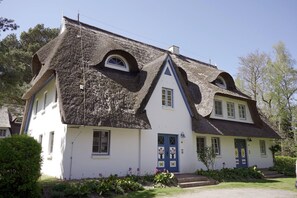 Une maison traditionnelle avec un toit à forte pente, une entrée centrale dotée d’une porte bleue et un petit porche.