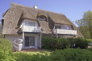 A thatched-roof house with a balcony and a covered porch.