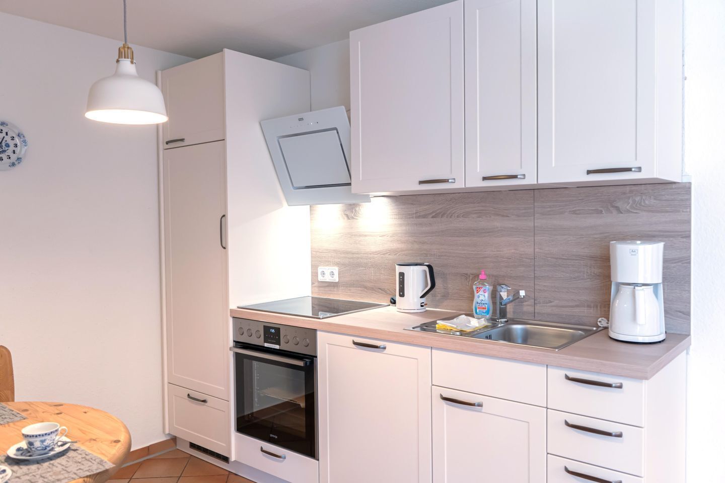 Una cocina compacta con armarios blancos, horno empotrado, microondas, cafetera y lavabo.