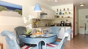 Un comedor con sillas de mimbre, una mesa redonda de cristal y una lámpara colgante azul.