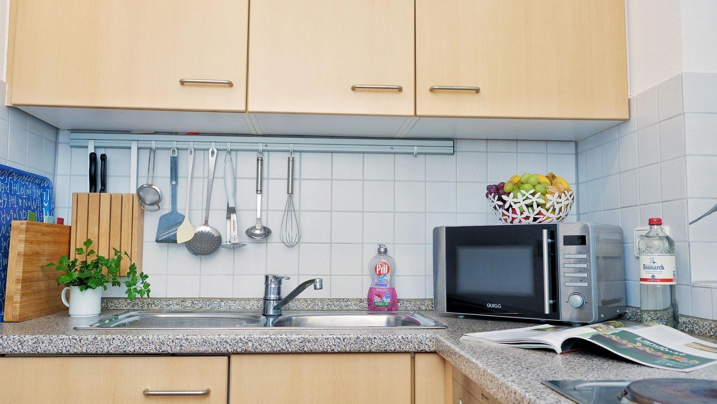Cozinha com pia, micro-ondas e diversos utensílios pendurados acima.