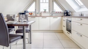 Una cocina moderna con comedor, que cuenta con tragaluz, armarios blancos y horno empotrado.