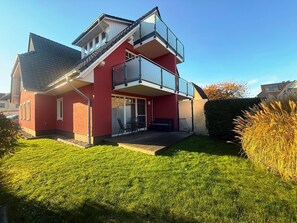 Une maison à deux étages avec une façade rouge, un balcon et un petit patio.
