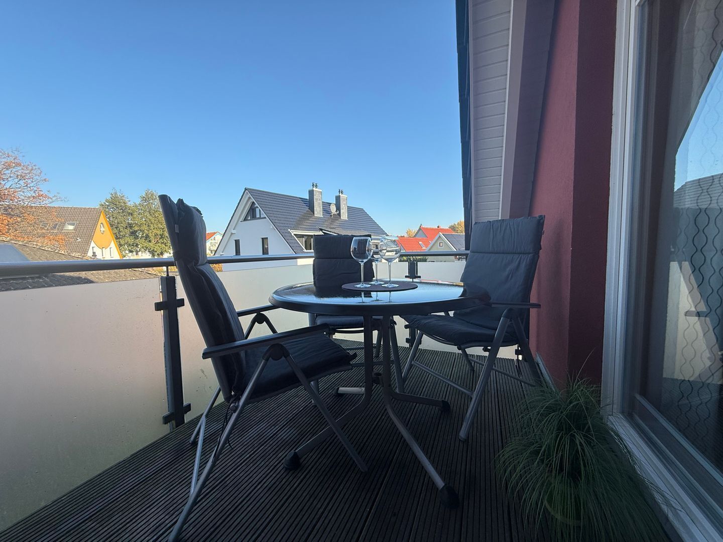 En balkon med to stole og et bord, en potteplante og udsigt til huse.