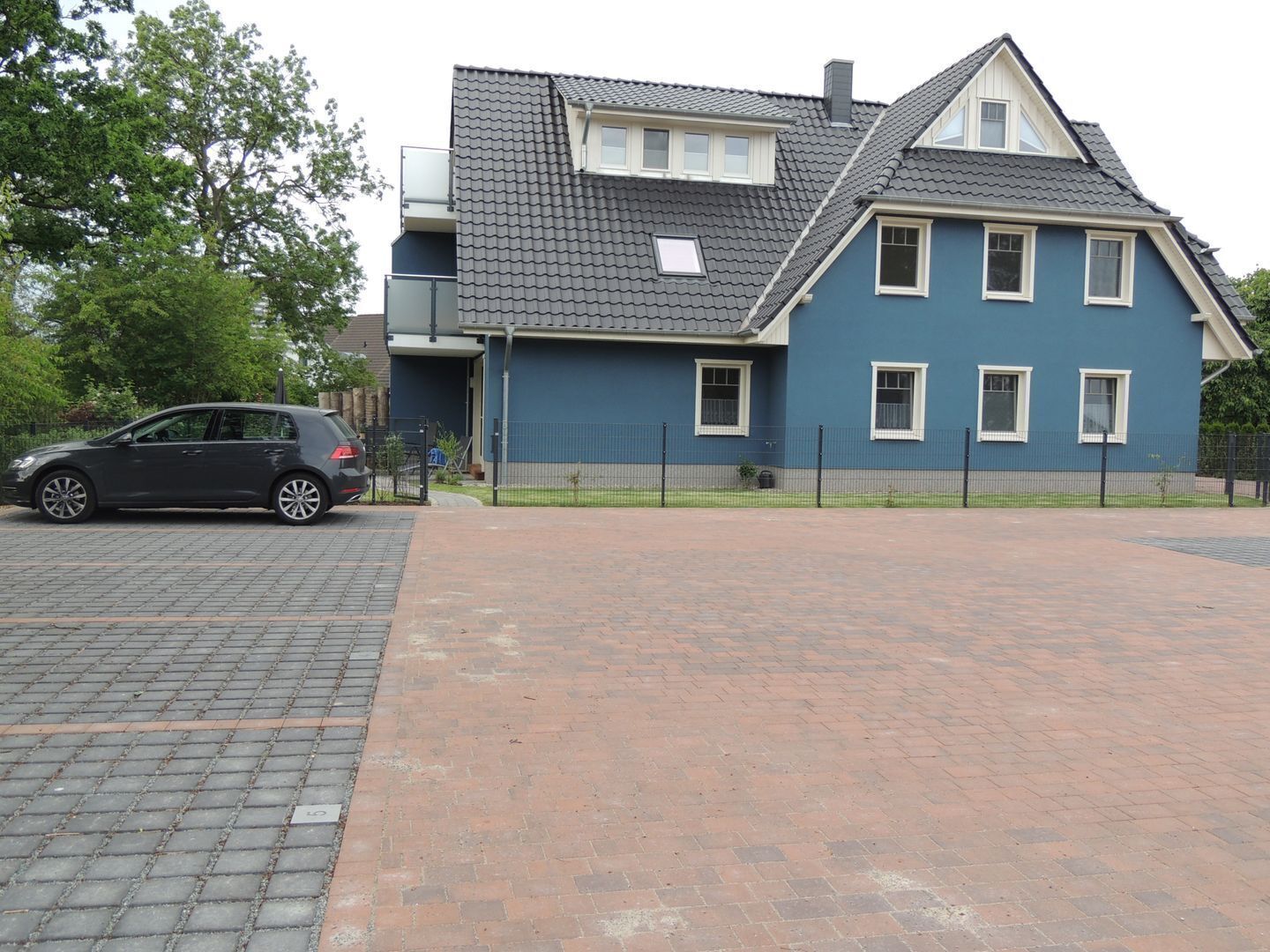 A two-story house with a grey tiled roof, a blue exterior, and a fenced driveway.