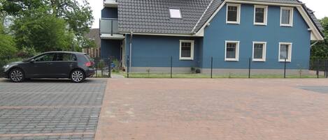 A two-story house with a grey tiled roof, a blue exterior, and a fenced driveway.