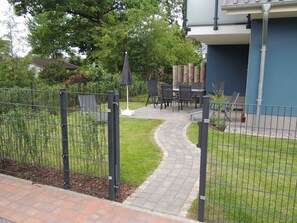 A fenced outdoor patio area with a curved pathway leading to a seating area with tables and chairs. - Helle, Freundliche Ferienwohnung in Strandnähe! - Kavelweg 13 (Zingst)