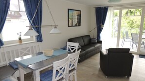 A modern living room with a dining area, featuring a sofa, chairs, a table, and a view of the outdoors. - Helle, Freundliche Ferienwohnung in Strandnähe! - Kavelweg 13 (Zingst)