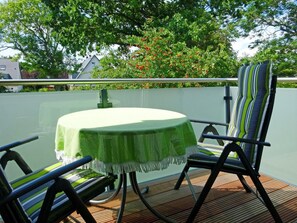 Ein runder Tisch mit grüner Tischdecke, zwei gestreifte Stühle und im Hintergrund ein Haus und Bäume.