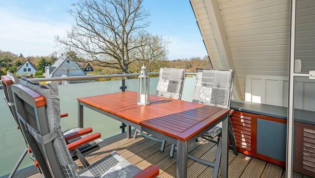 An outdoor deck with a table and chairs, a lantern, and a view of houses and trees. - Helle, Freundliche Ferienwohnung in Strandnähe! - Kavelweg 13 (Zingst)
