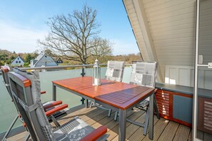 Um deck externo com mesa e cadeiras, um candeeiro e vista para casas e árvores.