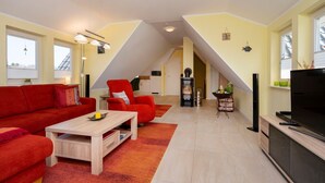 A modern living room with a red sofa, a wooden coffee table, and a TV stand. There is a fireplace and a small table with decorative items. - Helle, Freundliche Ferienwohnung in Strandnähe! - Kavelweg 13 (Zingst)