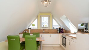 A modern kitchen with a dining area, featuring a wooden countertop, a built-in oven, and a window with a view. - Helle, Freundliche Ferienwohnung in Strandnähe! - Kavelweg 13 (Zingst)